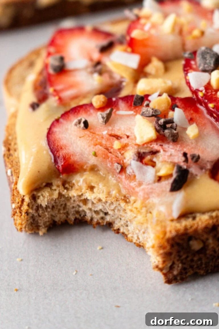 A slice of multigrain toast generously topped with creamy coconut peanut butter, garnished with fresh strawberry slices and a sprinkle of granola crumble.