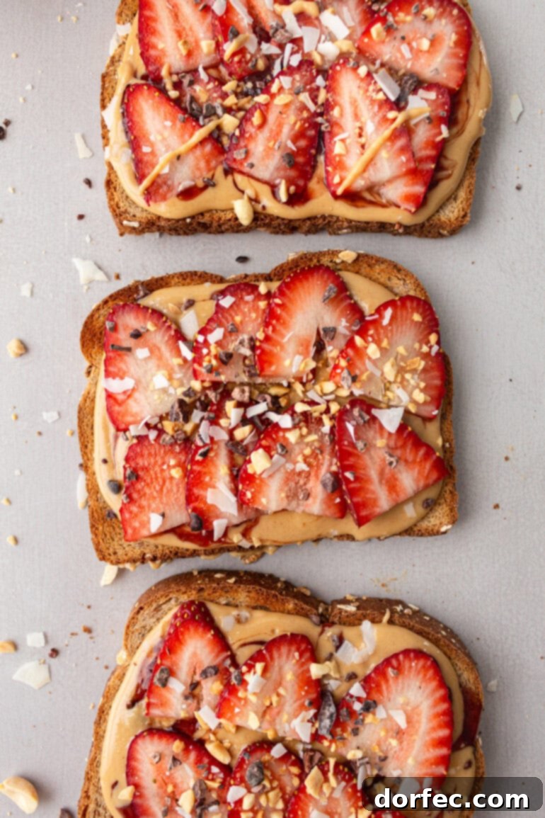 Three slices of whole-grain toast, each generously topped with coconut peanut butter and adorned with fresh strawberry slices, sprinkled with granola.