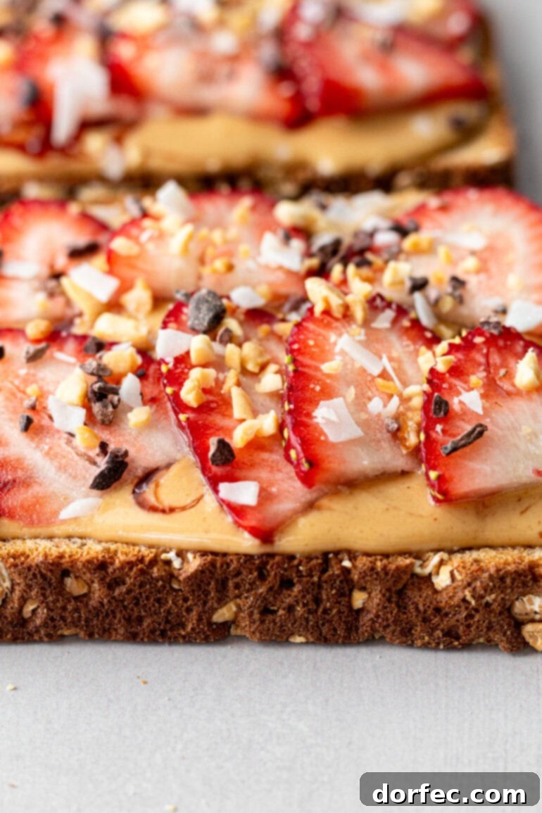 A slice of multigrain toast generously covered with coconut peanut butter, topped with sliced strawberries and sprinkled with granola for a delightful and wholesome snack.