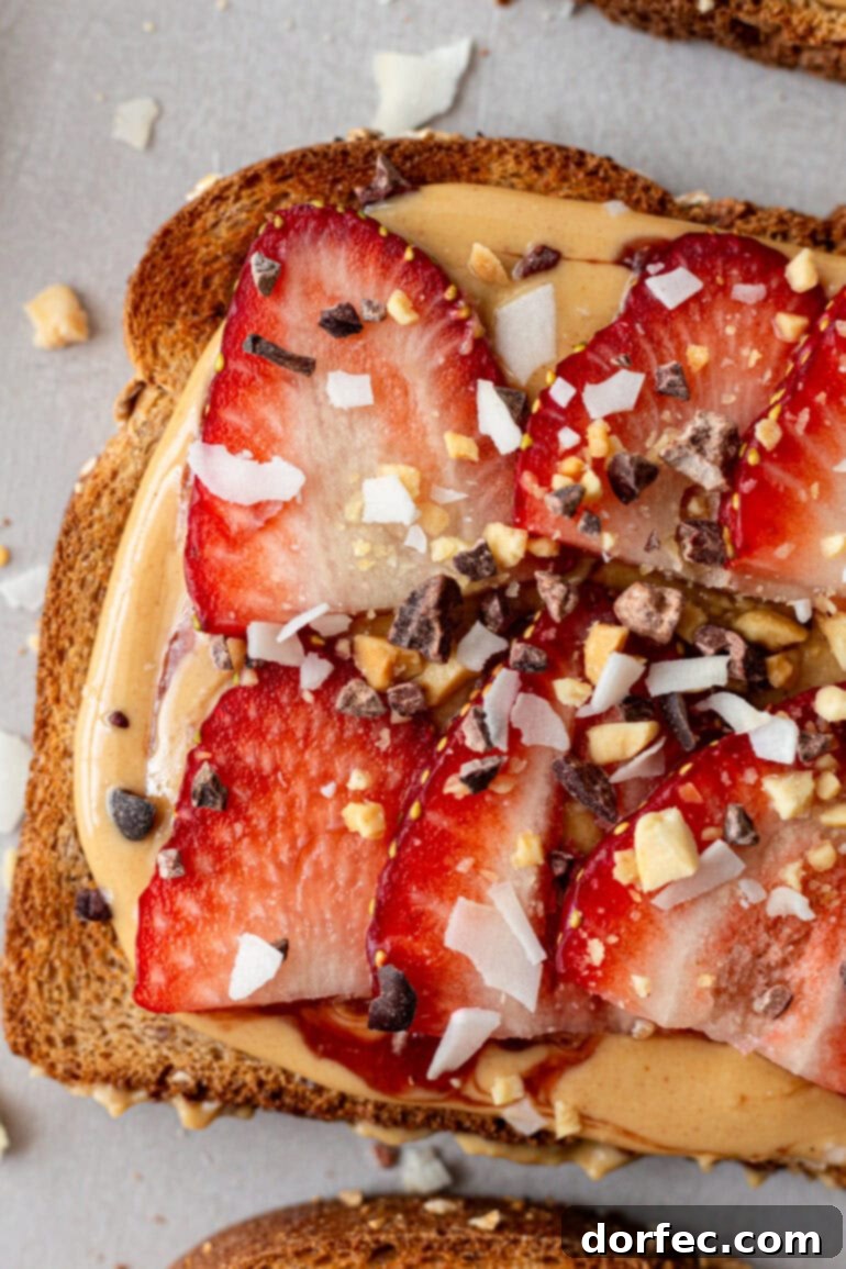 A piece of toast adorned with creamy coconut peanut butter, fresh strawberry slices, and a delightful sprinkle of chocolate bits, chopped peanuts, and coconut flakes.