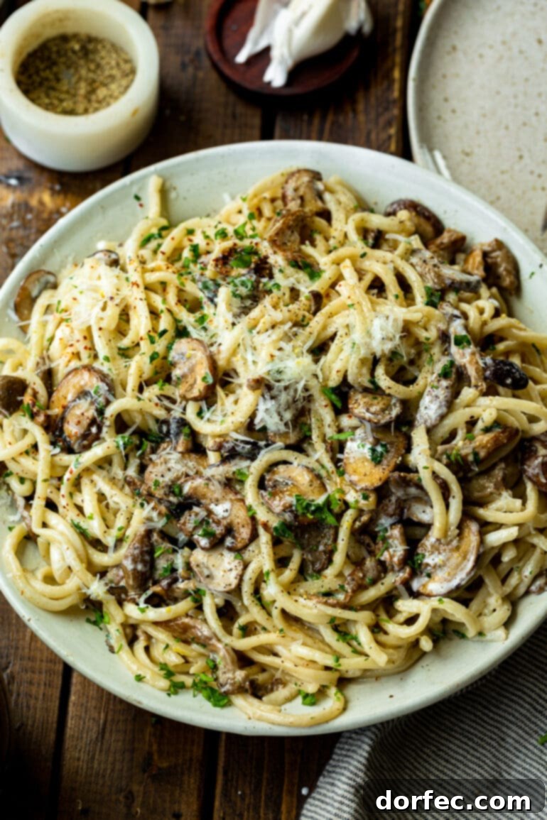 A large white serving plate filled with a generous portion of creamy mushroom pasta, garnished with fresh shaved Parmesan cheese and chopped green parsley, highlighting its rich and inviting texture.