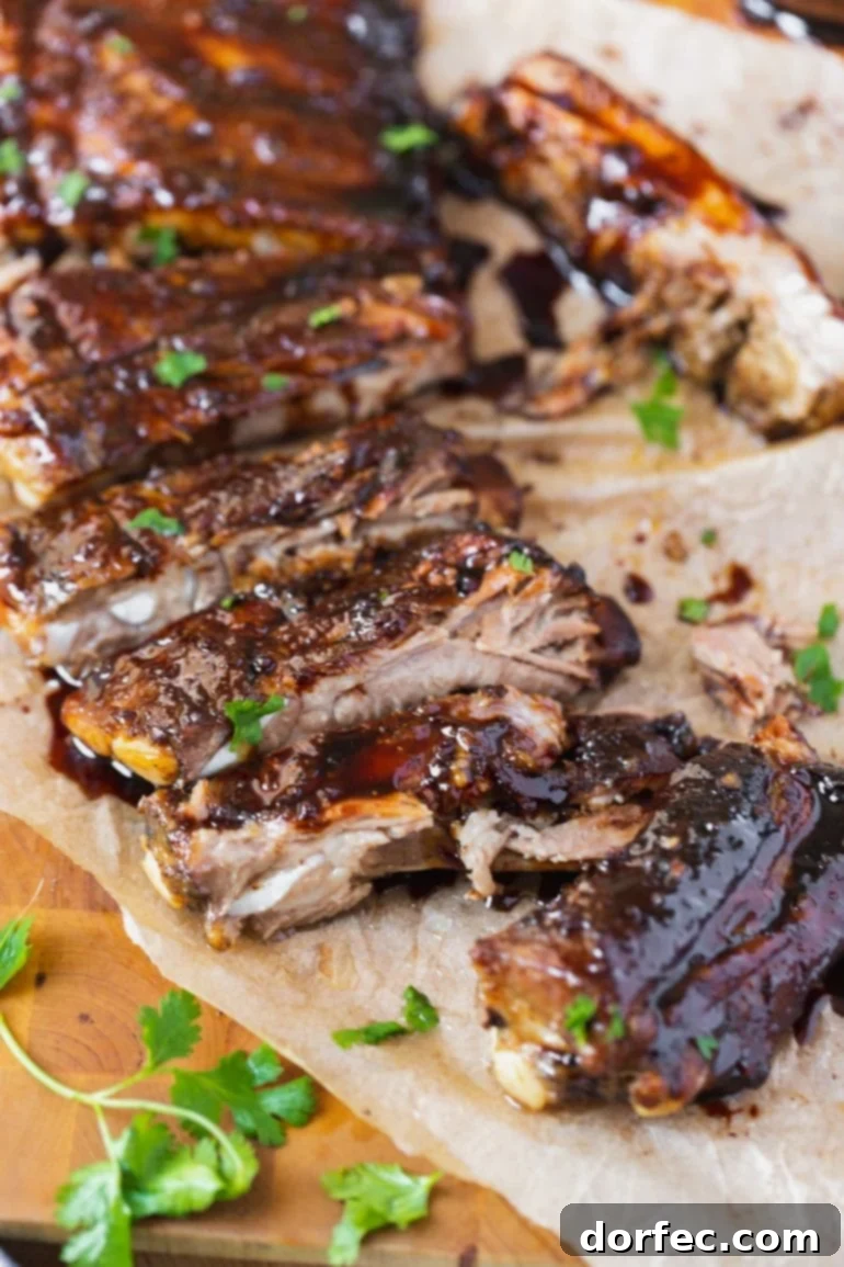 A beautifully presented rack of Asian sticky ribs, cut into individual portions, generously topped with toasted sesame seeds and freshly chopped cilantro, highlighting the rich, glossy glaze.