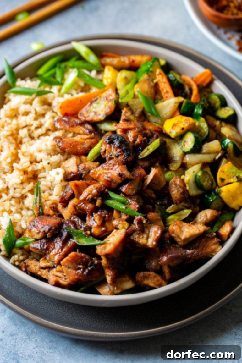 a photo of juicy flavorful bourbon chicken with a side of brown rice and sauteed vegetables.