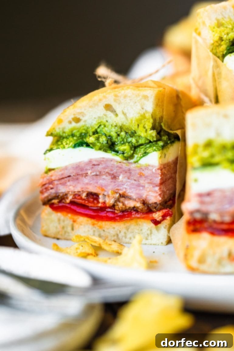 a close up photo of a pressed Italian sandwich stuffed with layers of meat, pesto, fresh mozzarella, roasted red pepper and tomato.
