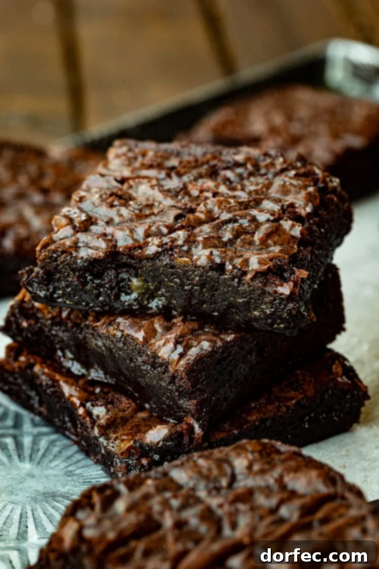 Decadent Box Mix Brownies 2 A photo of three intensely chocolatey brownies stacked on each other, showcasing their signature crinkly tops and rich texture, perfect for any chocolate lover.