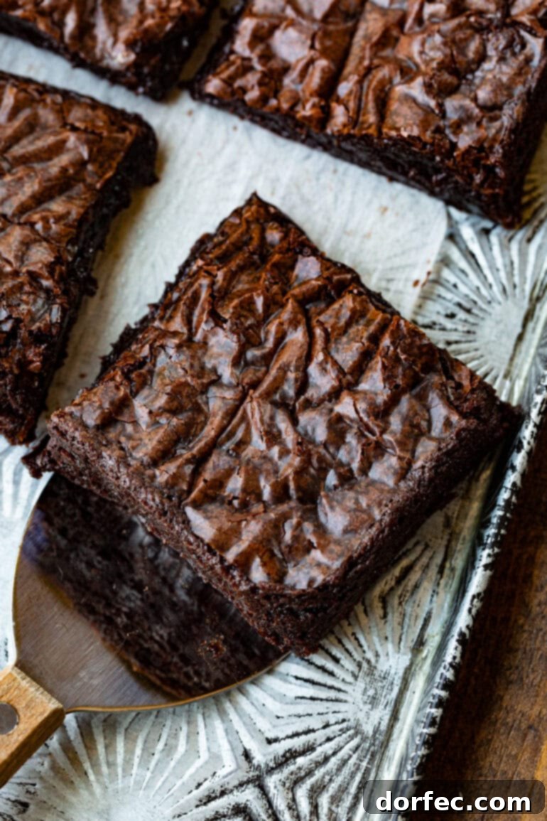 Decadent Box Mix Brownies 3 A photo taken from above, showing a square chocolate brownie being carefully lifted from a pan of freshly baked brownies with a small metal spatula, highlighting its rich, dark color and perfect shape.