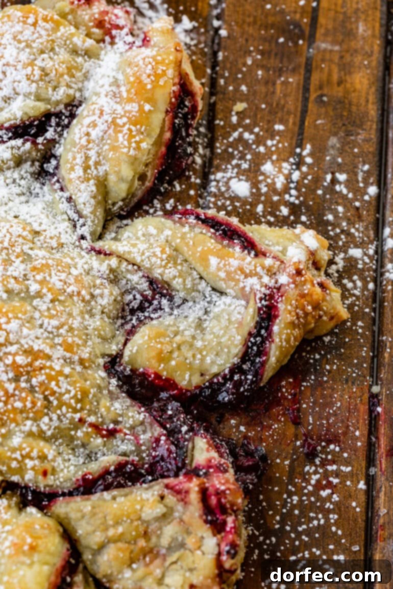 A close-up view of one twisted arm of a baked Blackberry Puff Pastry Snowflake, showcasing the flaky pastry and berry filling.