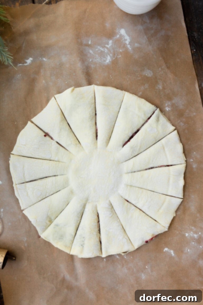 A sheet of unbaked puff pastry dough, cut into a perfect circle with a central indentation and 16 radial strips for a snowflake design.
