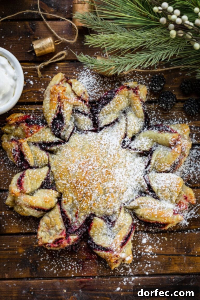 Overhead view of a shimmering golden-baked Blackberry Puff Pastry Snowflake, generously dusted with powdered sugar, creating a festive winter wonderland effect.
