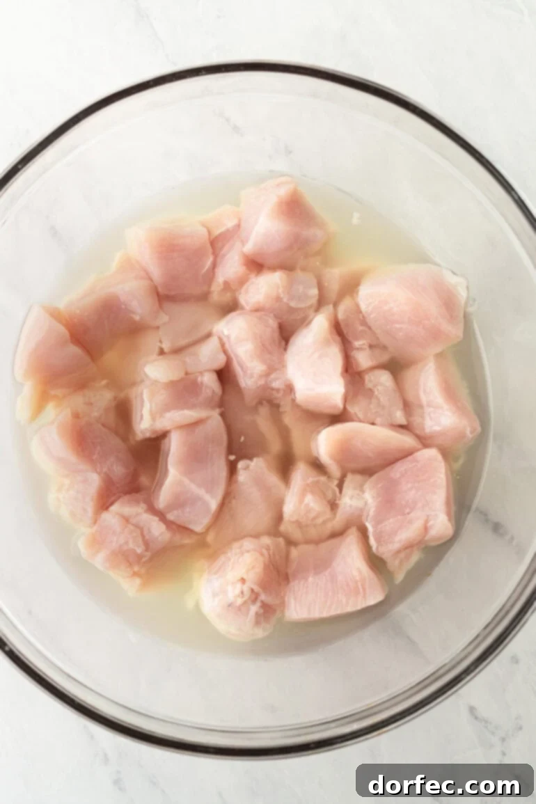 Raw chicken pieces marinating in pickle juice, showing the crucial brining step for tender and flavorful Chick-fil-A copycat nuggets.