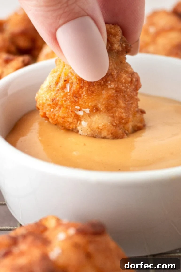 A close-up shot of a hand dipping a golden, crispy chicken nugget into a bowl of creamy orange sauce, emphasizing the delicious pairing of the homemade Chick-fil-A style nugget with its secret sauce.