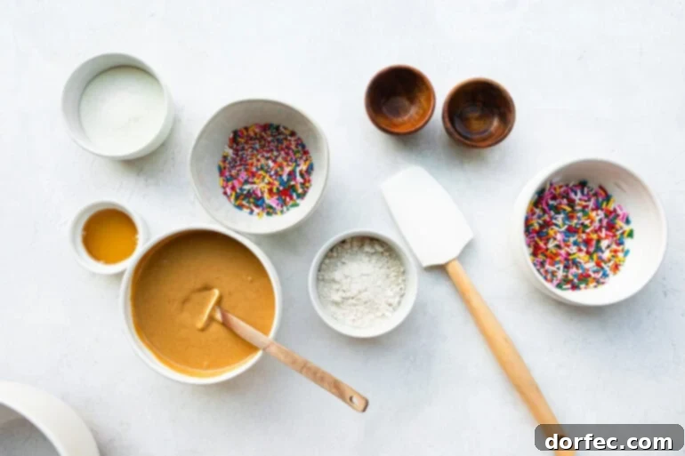 A top-down photo showcasing all the individual ingredients for no-bake cake batter protein bites, neatly arranged in small white bowls on a light surface.