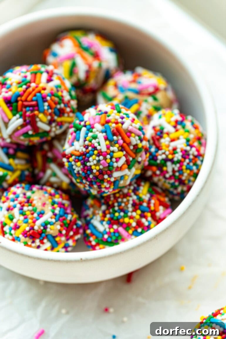 A beautiful photo of several protein balls, generously coated in colorful rainbow sprinkles, neatly arranged in a clean white bowl.