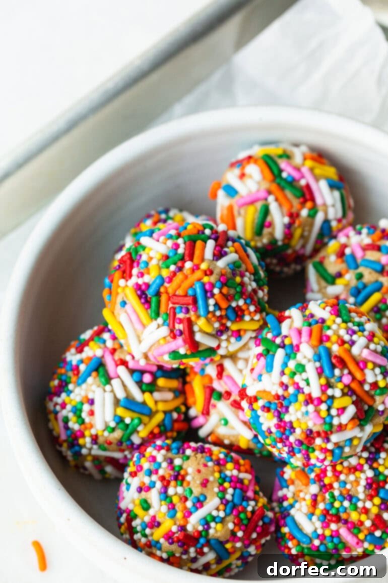 A vibrant photo of a bowl filled with colorful cake batter protein bites, generously covered in rainbow sprinkles, ready for serving.