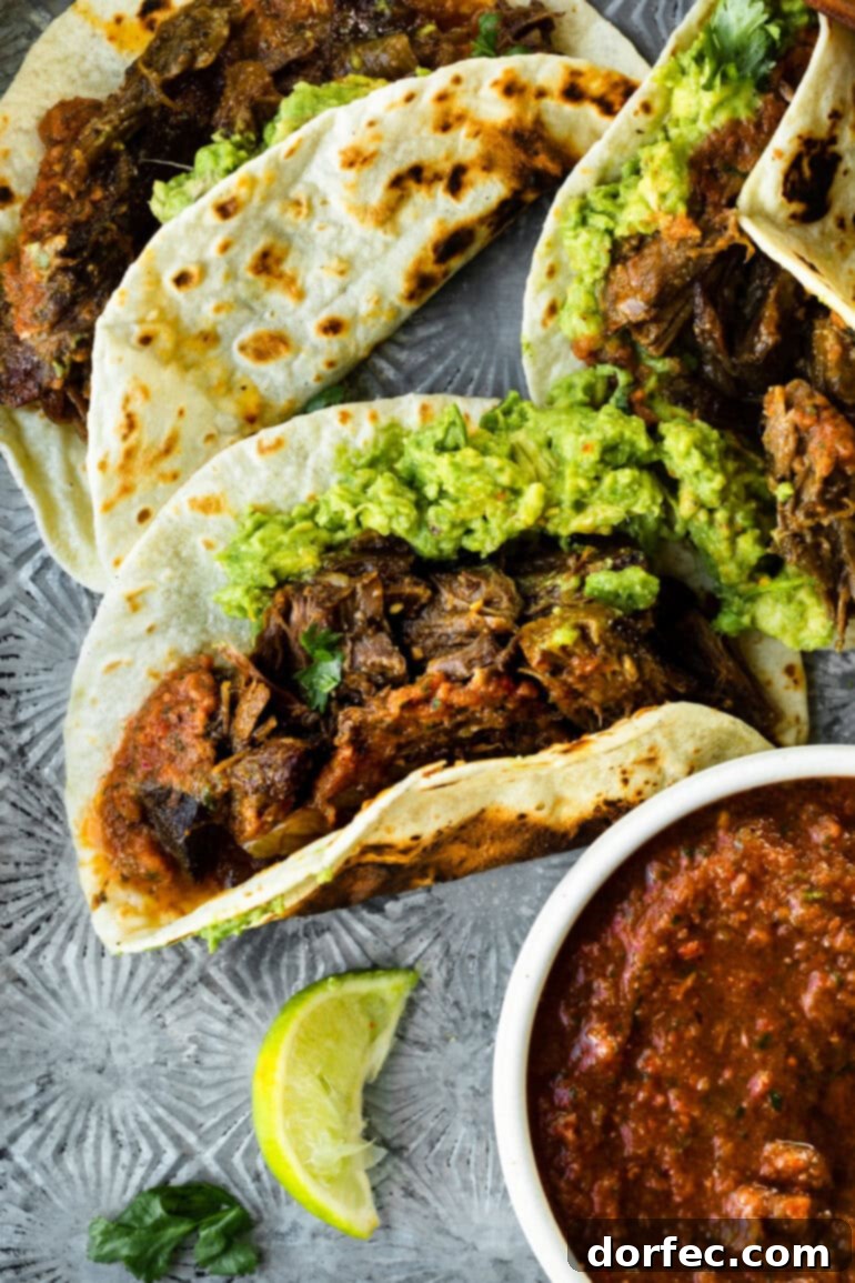 A close-up photo of a beautifully assembled shredded beef taco on a warm flour tortilla, generously topped with fresh guacamole and a sprinkle of cilantro.
