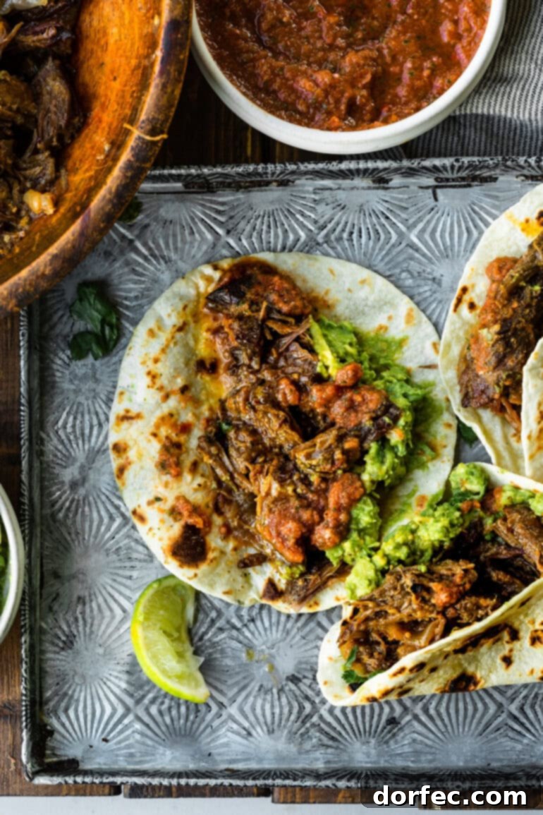A captivating photo of several beautifully prepared shredded beef tacos on soft flour tortillas, artfully arranged on a rustic baking sheet with a small bowl of fresh guacamole, ready to be devoured.