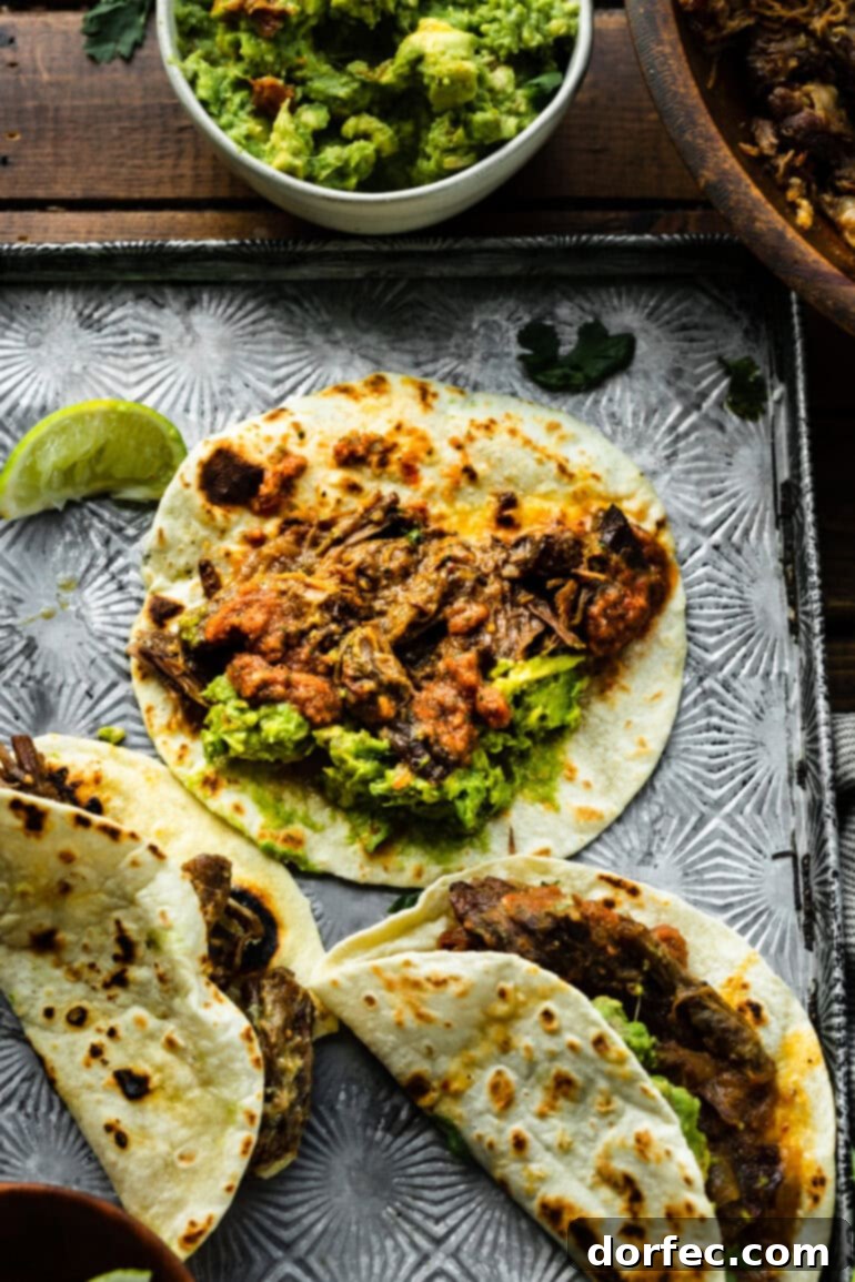 A simple yet enticing shot of a few shredded beef tacos on warm flour tortillas, resting on a sheet pan, ready to be garnished and served.