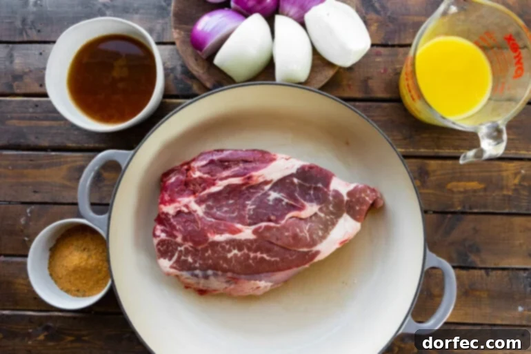 A vibrant flat lay photo displaying all the fresh ingredients for shredded beef tacos: a raw boneless chuck roast, quartered red and yellow onions, a glass of orange juice, a carton of beef stock, and a bottle of Kinder's Carne Asada Rub.