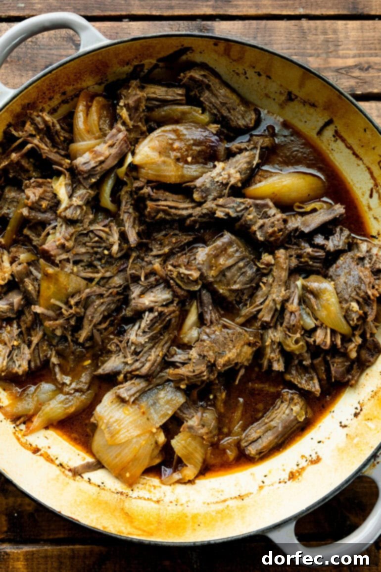 Close-up of shredded beef in a Dutch oven, showing its tender texture after slow cooking.