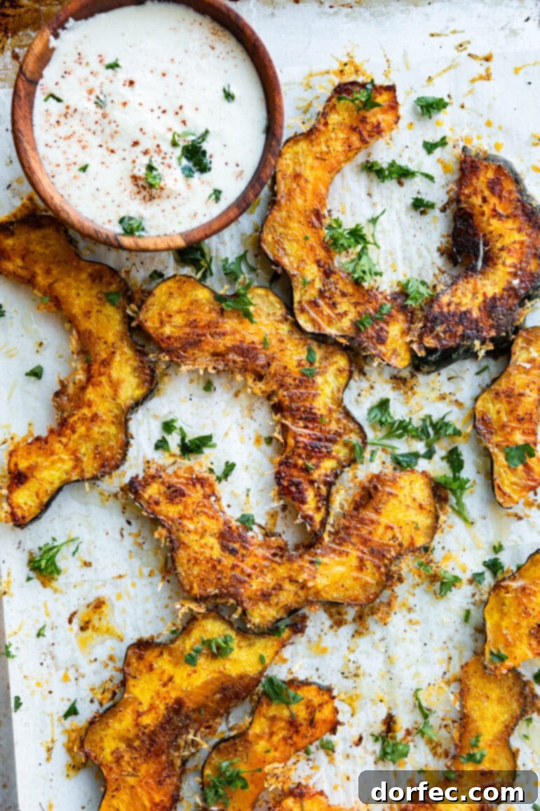 A photo showcasing several vibrant slices of roasted acorn squash, beautifully topped with a golden, crispy cheese and herb crust, alongside a small bowl of creamy dip, ready to be enjoyed as a comforting fall meal.