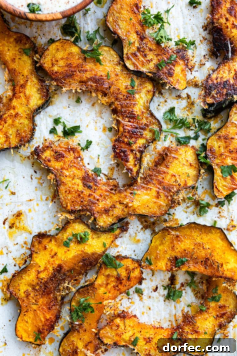 A close-up shot of several slices of roasted acorn squash, each piece perfectly coated in crispy, golden-brown cheese and fragrant herbs.