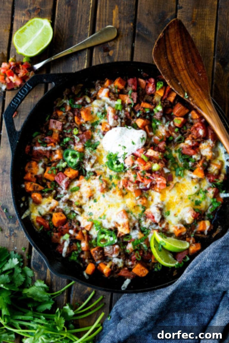 A close-up photo of a cast iron skillet brimming with the fully cooked cubed sweet potatoes and seasoned taco ground beef mixture.