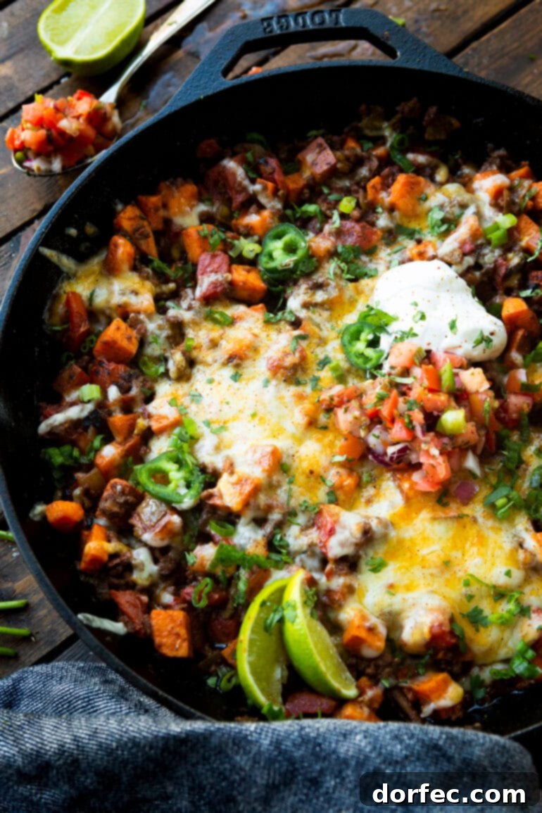 A rustic cast iron skillet filled with a hearty ground beef taco and sweet potato hash, artfully garnished and ready to be served.