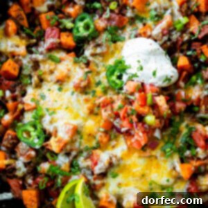 A photo of a cast iron skillet full of taco ground beef and diced sweet potatoes topped with a dollop of sour cream, chopped fresh cilantro and lime wedges
