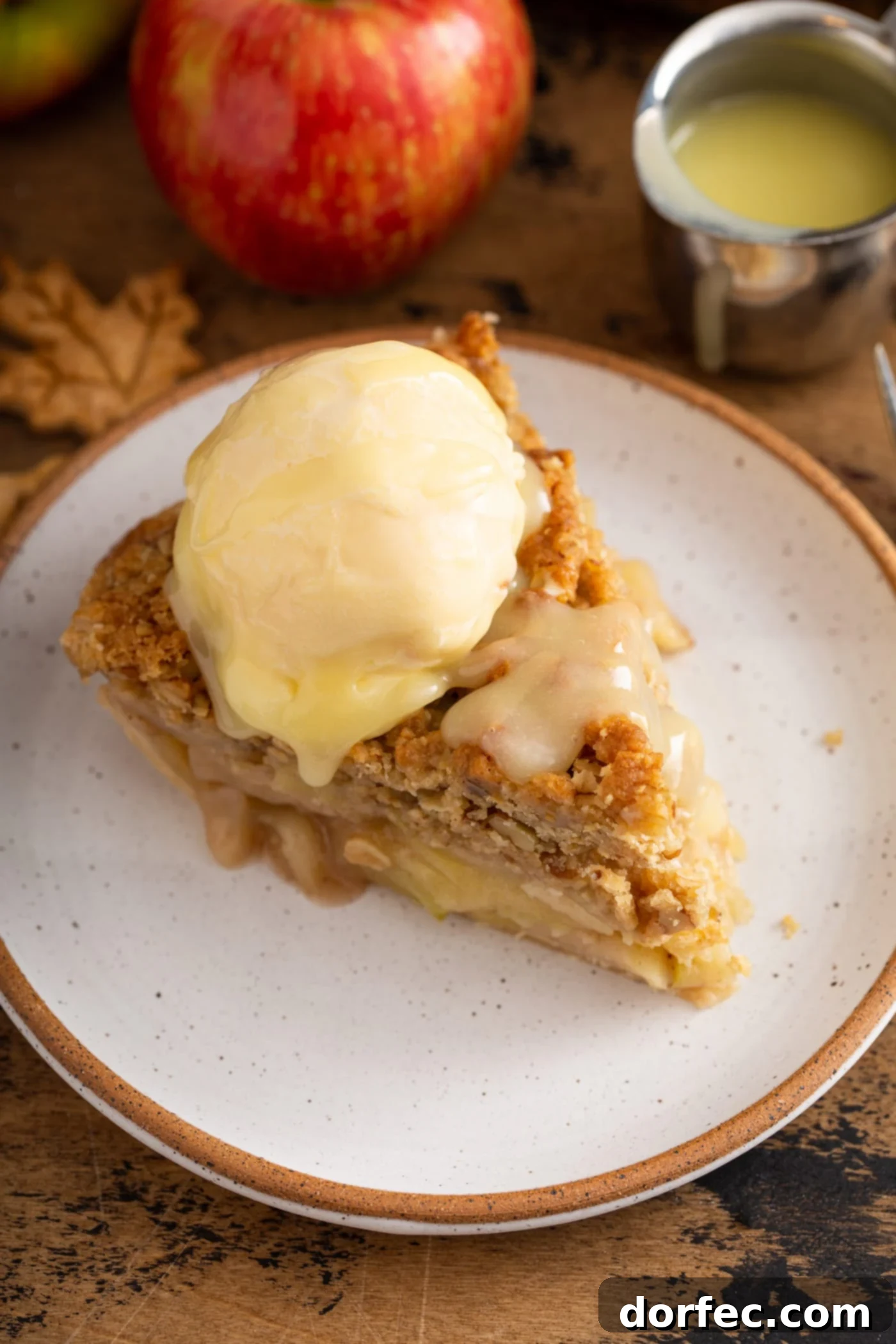 A close-up of a delightful slice of Dutch apple pie, crowned with a scoop of vanilla ice cream and generously drizzled with a rich white chocolate butter sauce, showcasing its inviting textures and flavors.