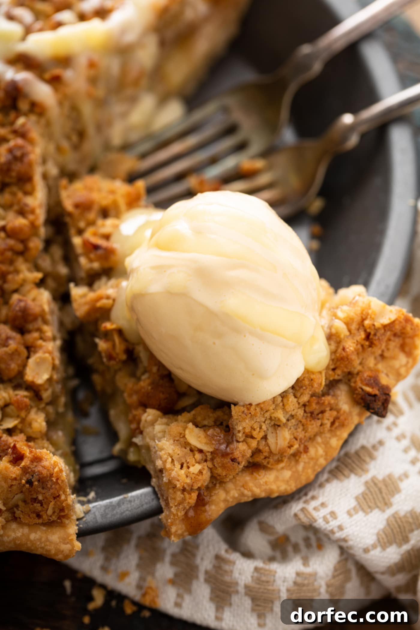 A mouthwatering slice of Dutch apple pie being carefully lifted from the pie dish, topped with a melting scoop of vanilla ice cream and gracefully drizzled with white chocolate butter sauce, ready to be savored.