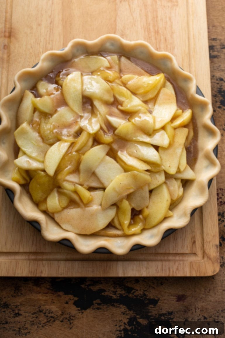 A golden pastry shell generously filled with partially cooked sliced apples, brown sugar, melted butter, and fragrant spices, ready for the crumble topping.