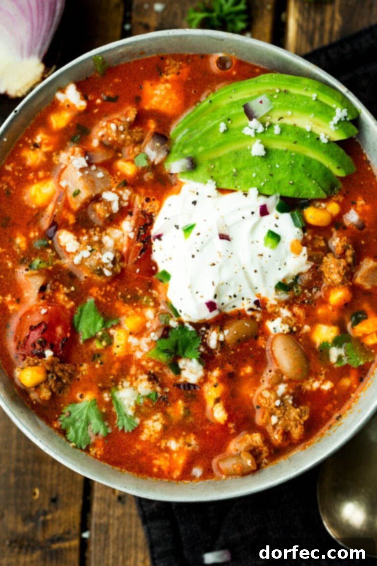 A bowl of charro bean soup topped with sour cream and sliced avocados
