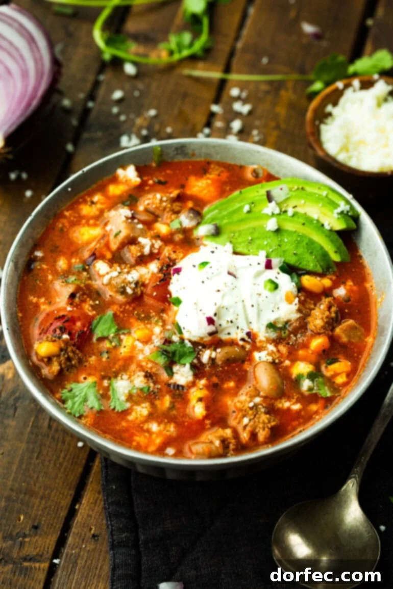 A bowl of hearty charro bean soup topped with sour cream, sliced avocados, and chopped cilantro