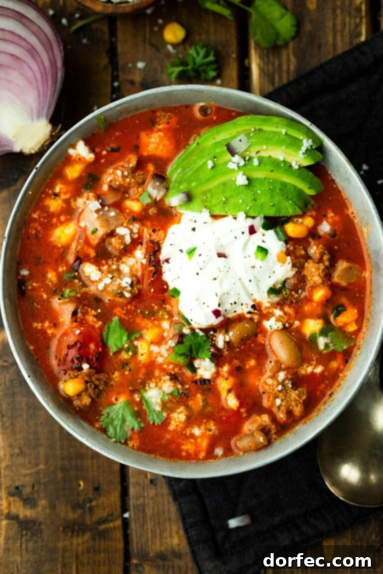 A bowl of charro bean soup with pinto beans, corn, chorizo, bacon, and sour cream and avocado toppings