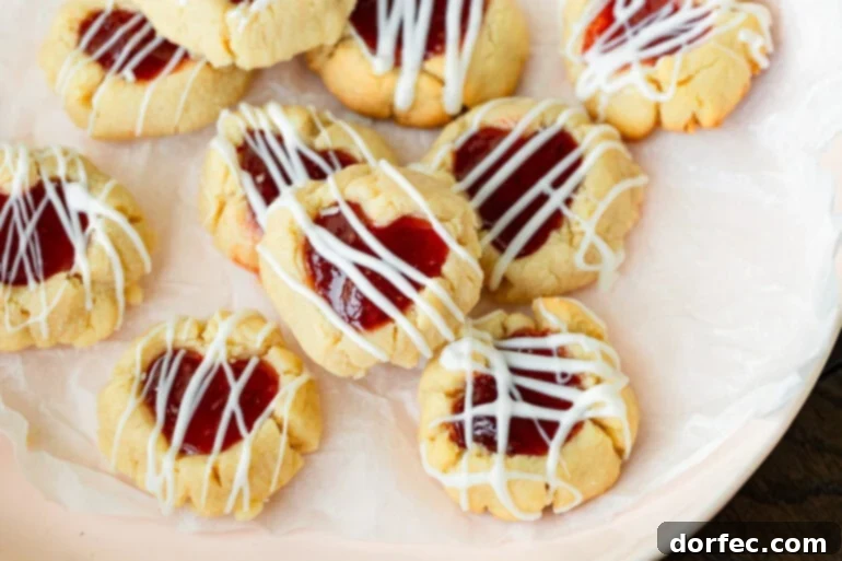 Valentine's Day thumbprint cookies arranged on a plate with jam-filled centers and white chocolate drizzle.