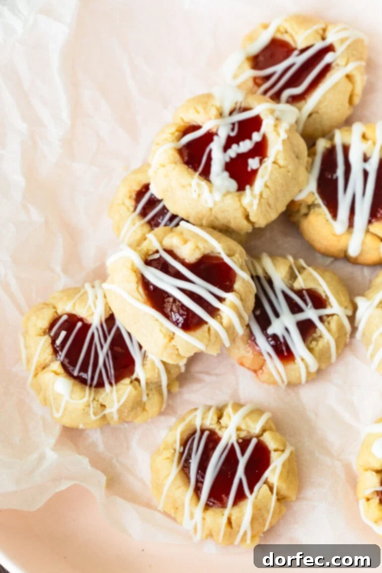 Several Valentine's thumbprint cookies filled with dark red jam and drizzled with melted white chocolate