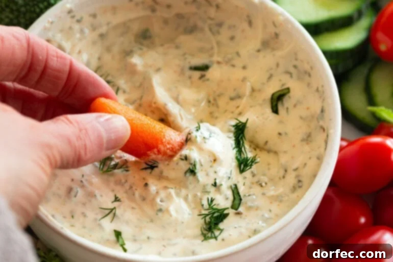 Creamy Herb and Garlic Vegetable Dip 7 Someone dipping a baby carrot in creamy garlic herb veggie dip