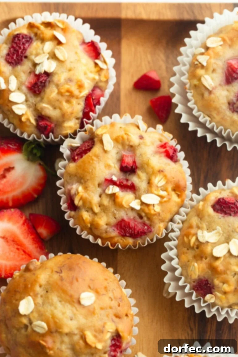 A top-down view of several golden-brown healthy strawberry oat muffins with visible oats and strawberry pieces, set on a rustic surface.
