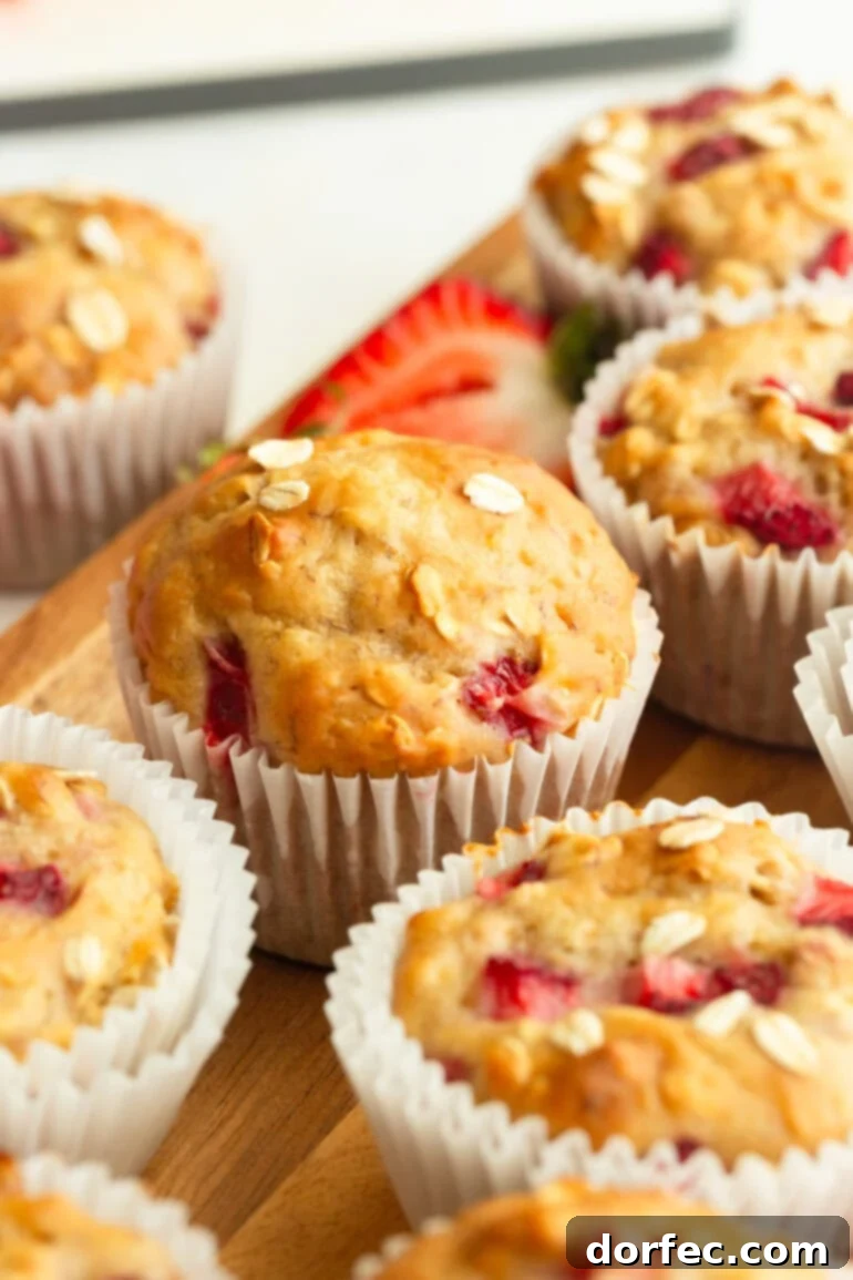 A close-up shot of a single healthy strawberry oat muffin, showcasing its fluffy texture, golden crust, and visible pieces of fresh strawberry and oats.