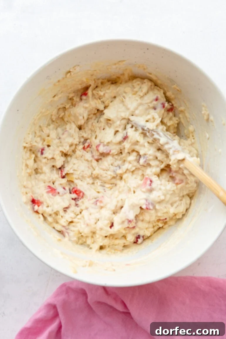 A large mixing bowl filled with the prepared healthy strawberry oat muffin batter, showing the visible oats and diced strawberries.