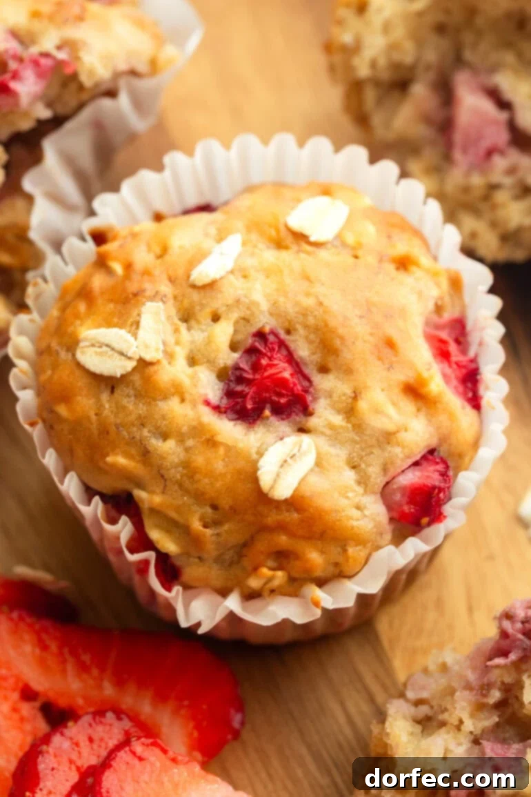A close-up image of a single healthy strawberry oat muffin, showcasing its golden crust, soft interior, and generous chunks of fresh strawberries.