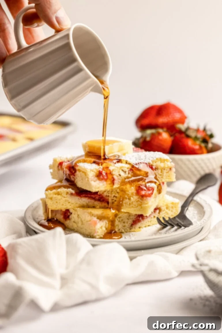 One Pan Strawberry Pancakes 13 Someone pouring a generous stream of golden maple syrup over a stack of warm strawberry sheet pan pancakes.