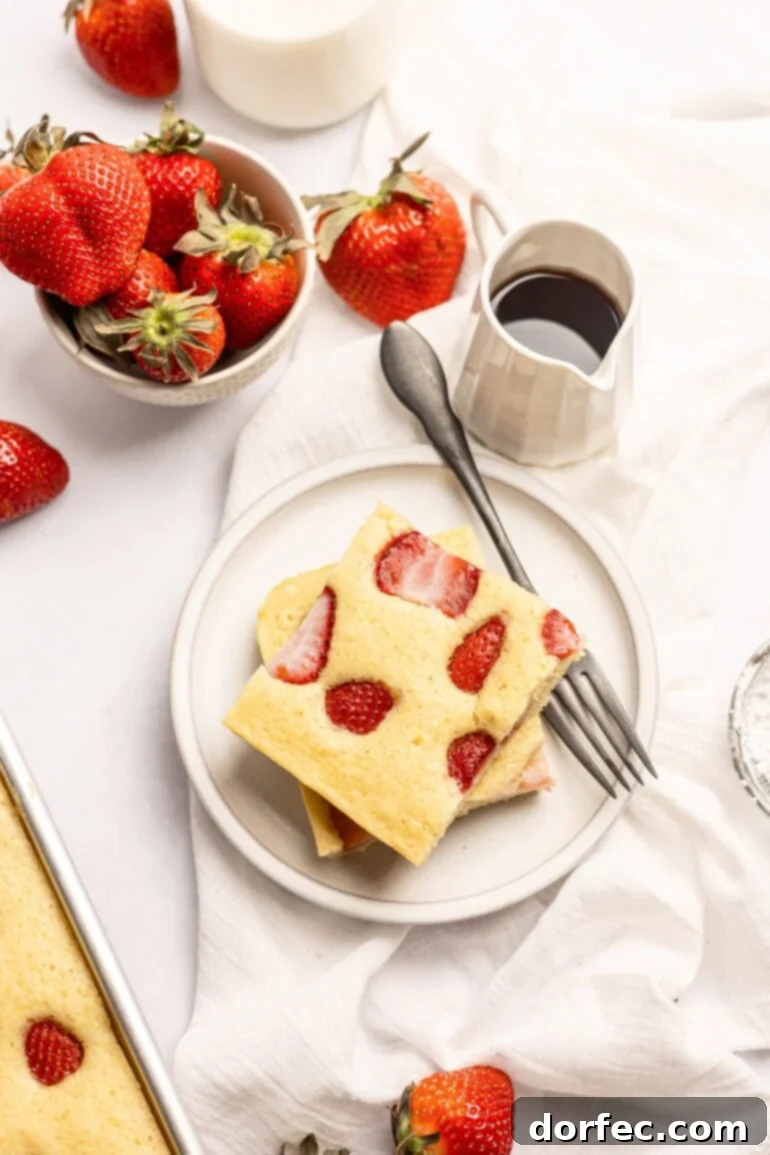 One Pan Strawberry Pancakes 5 Two generous slices of strawberry sheet pan pancakes stacked on a white plate, accompanied by a fork.