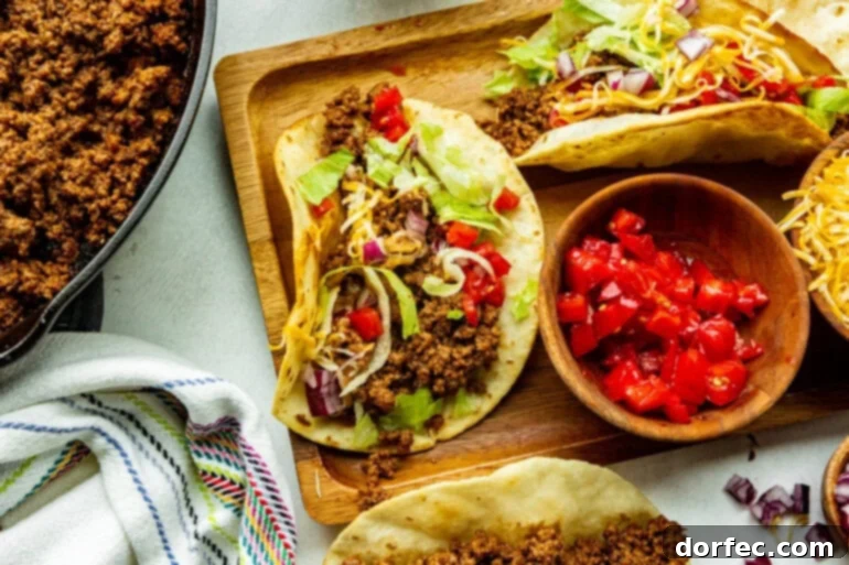 A wooden board topped with perfectly seasoned ground beef tacos nestled in warm corn tortillas, garnished with fresh cilantro and lime wedges.