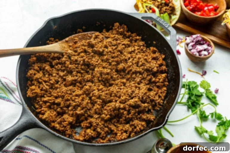 A cast iron skillet filled with deliciously seasoned and saucy ground beef, being stirred with a wooden spoon, ready to be scooped into taco shells.