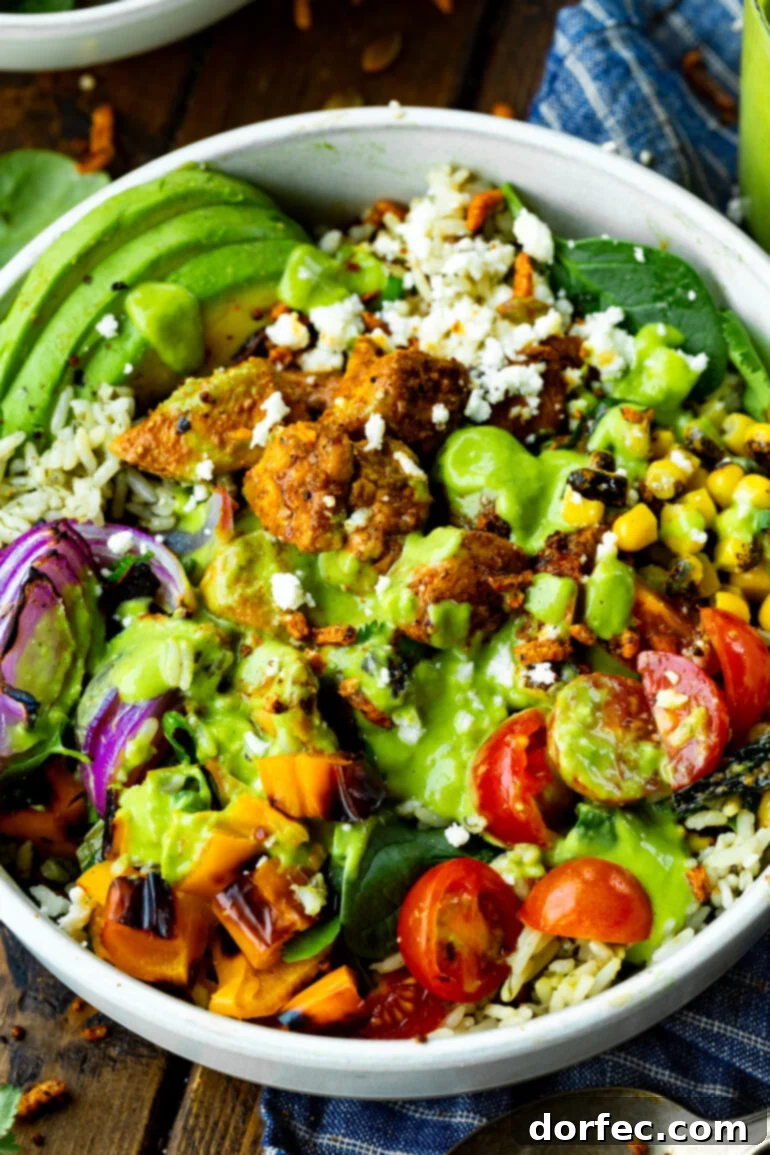 A colorful Mexican chicken burrito rice bowl, generously topped with halved cherry tomatoes, sweet corn, red onion, crumbled queso fresco, perfectly seasoned chicken chunks, and a creamy avocado dressing.