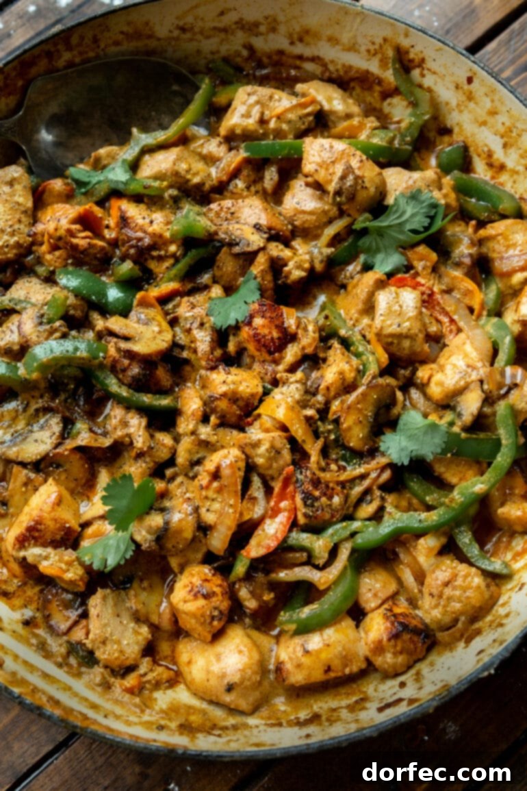 A delectable photo of a large skillet brimming with golden chicken chunks, perfectly mixed with sautéed green bell peppers, onions, and mushrooms, all bathed in a creamy sauce.