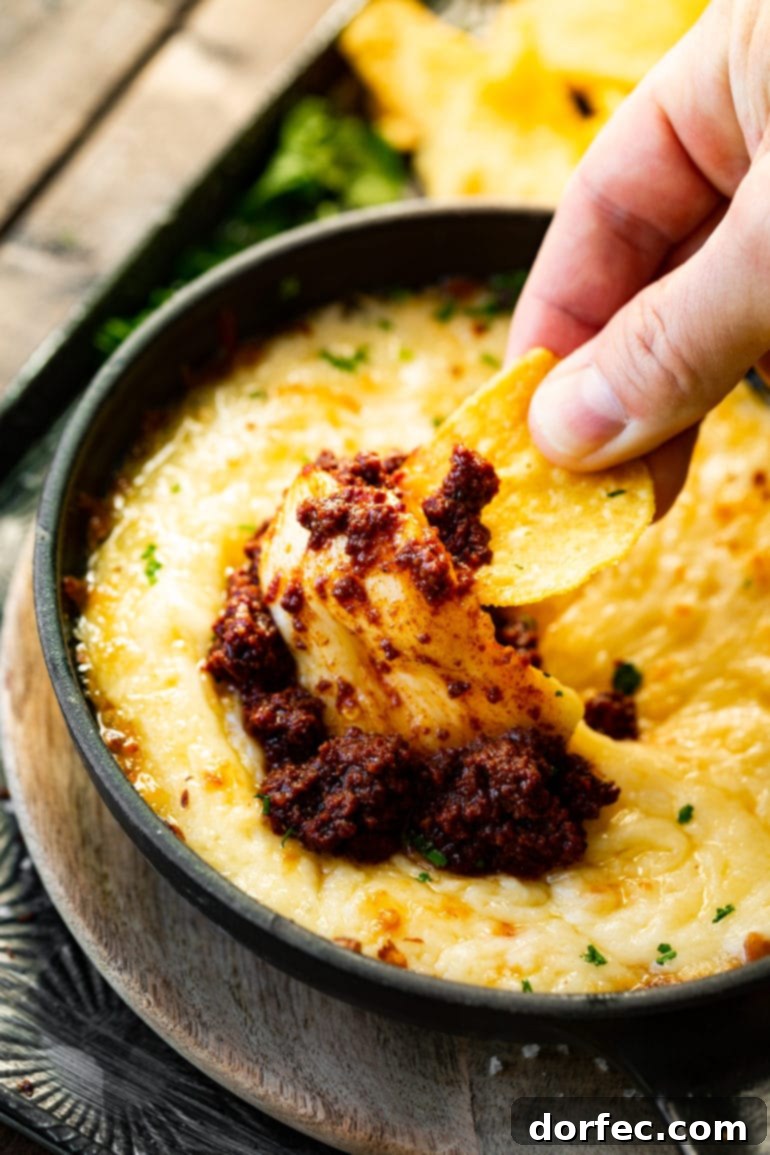 A mouthwatering photo of someone using a tortilla chip to scoop up a generous bite of sizzling Chorizo Queso Fundido, highlighting its gooey texture.