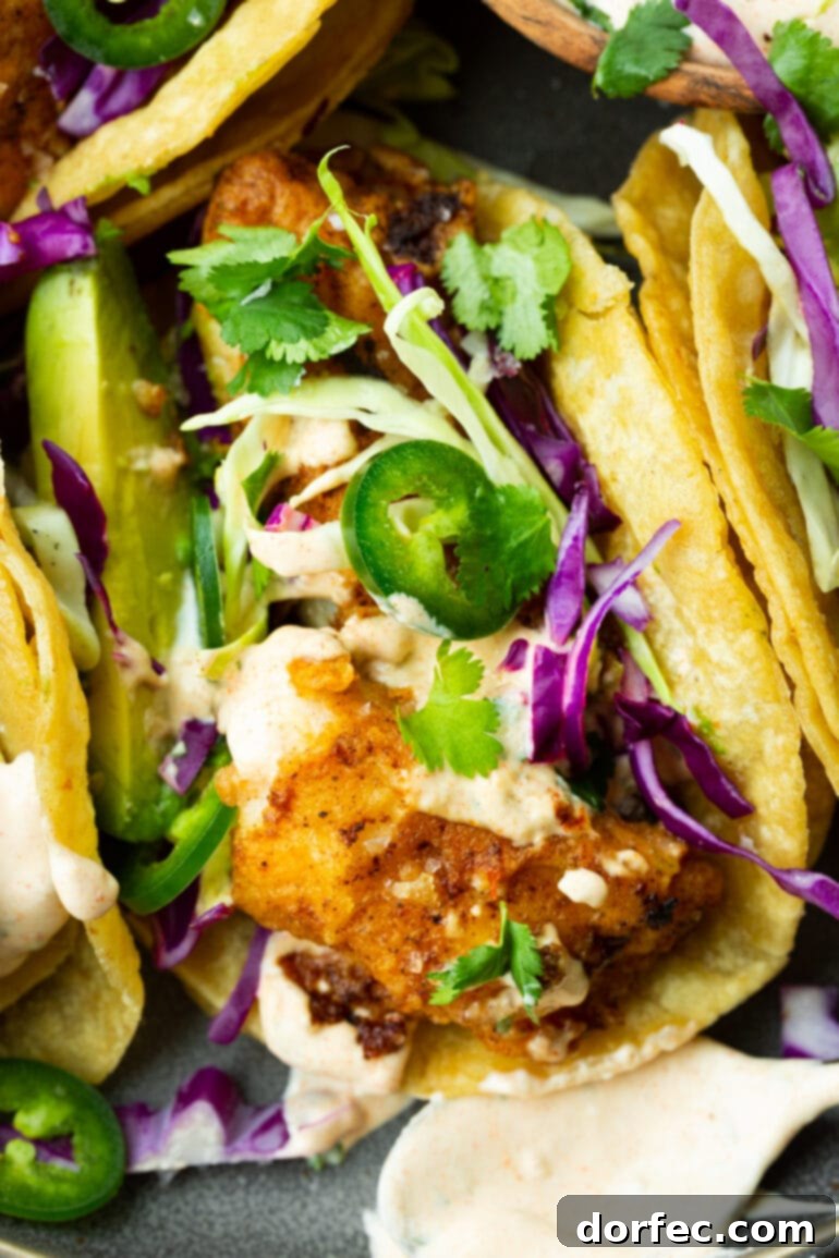 A delicious fish taco featuring golden, tender fish, topped with crisp shredded cabbage, spicy jalapeño slices, fresh chopped cilantro, and a creamy taco sauce.