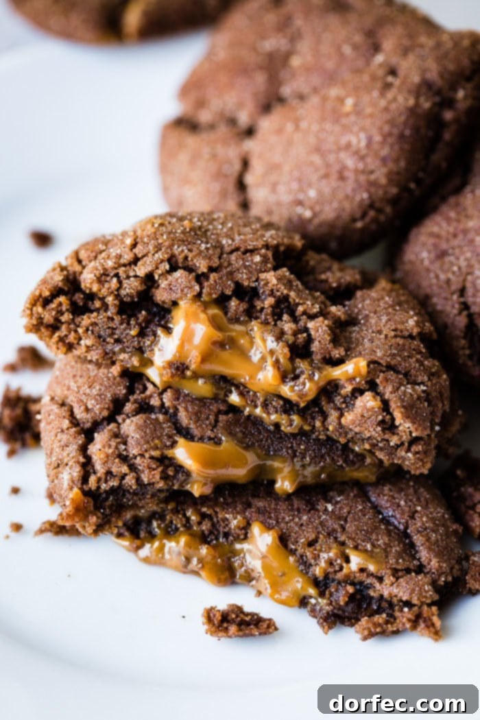 A delectable photo of three Dulce de Leche Stuffed Chocolate Mexican Cookies, halved and stacked to showcase the gooey dulce de leche oozing from the center, with whole cookies piled invitingly in the background.